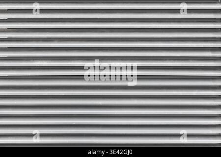 Close-up of horizontal metal shutters forming repetitive louvered panels in neutral gray tones, emphasizing industrial texture, shadow lines and minim Stock Photo