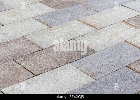 Textured stone paving on an urban walkway, featuring staggered rectangular gray and beige tiles forming a repeating geometric pattern for architectura Stock Photo