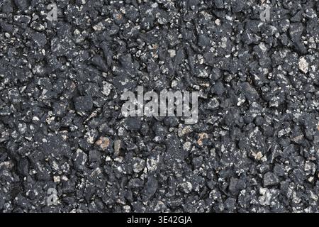 Close-up view of weathered asphalt pavement showing rough gravel, aggregate and cracks. A textured blacktop surface ideal for backgrounds, design over Stock Photo