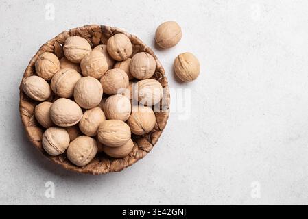Whole Walnuts In Round Wicker Basket on white concrete background, top view, copy space. Basket of walnuts. Stock Photo