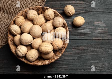 Whole Walnuts In Round Wicker Basket on dark wooden  background, top view, copy space. Basket of walnuts. Paleo diet and healthy eating concept. Stock Photo