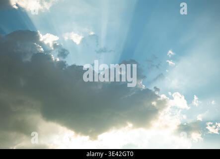 Sun shining through clouds creating crepuscular rays in a bright blue sky Stock Photo