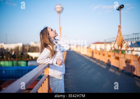 Young woman enjoying golden hour on city bridge, thinking about future Stock Photo