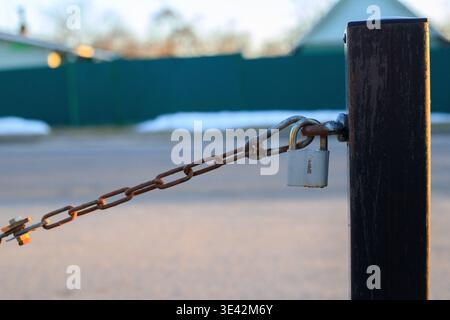 Close-up of a metal chain with a padlock attached to a pole at sunset. Concept of protection and security measures. Stock Photo