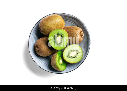 Kiwi fruits in blue bowl isolated on white background, top view, design element. Whole fruit and half pieces of green kiwi close up. Fresh ripe kiwi. Stock Photo