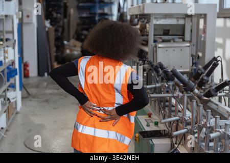 African American female industrial worker having physical workload and back pain while checking machinery, workplace injury in manufacturing Stock Photo