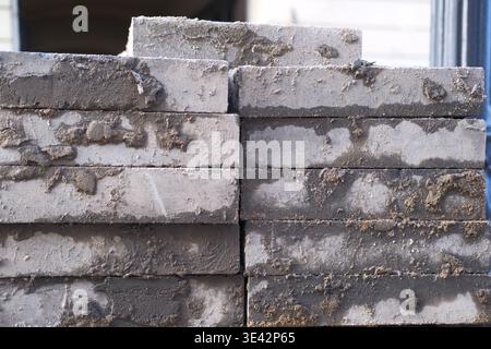 Stack of concrete blocks, pavers or bricks with dried mortar residue on them. Construction materials, street or sidewalk renovation. City maintenance Stock Photo