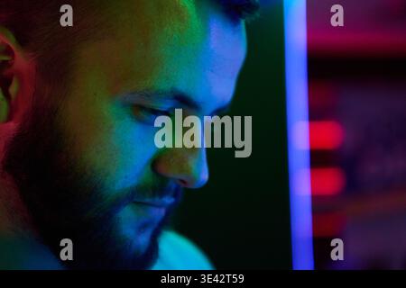 Contemplative Bearded Man Portrait in Colorful Neon Lighting Looking Down at Screen Stock Photo