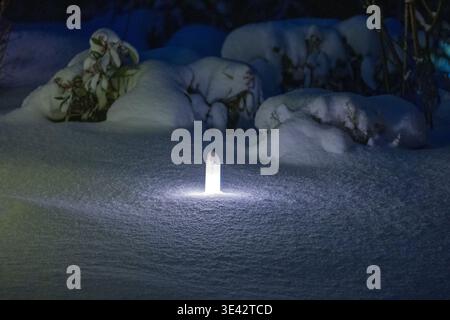 a brightly lit ground lamp in a snow-covered garden at night Stock Photo