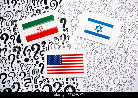 Three cards showing flags of IRAN, ISRAEL, and USA rest on background of hand drawn question marks. USA Israel Iran, Middle East crisis, trilateral Stock Photo