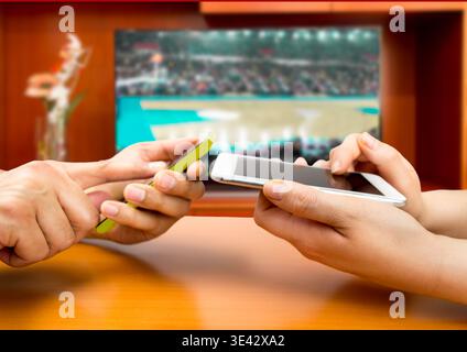 Friends using mobile phone and betting during a basketball match.With a tv background and an image of a basketball match Stock Photo