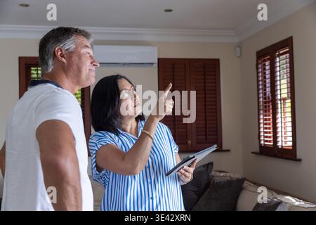Senior couple pointing and examining split air-conditioning unit in living room with tablet Stock Photo