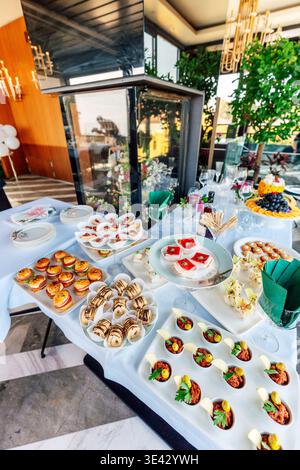 Sunlit Buffet With Assorted Canapes And Floral Centerpieces On Terrace Creating Festive Outdoor . Stock Photo