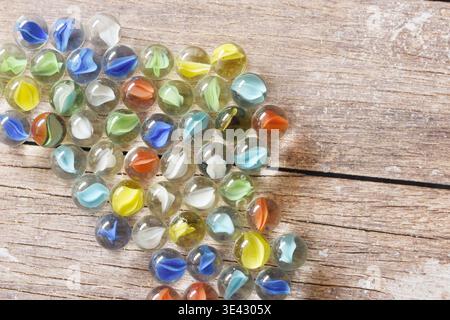 Transparent glass marbles scattered across a rustic wooden table with vibrant colorful background. Artistic composition with reflections, textures Stock Photo