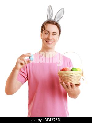 Smiling young man in bunny ears holding a painted Easter egg and a basket of colorful eggs on a white background. Happy spring holiday celebration con Stock Photo