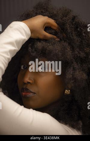 Close-up portrait of a woman with a voluminous curly afro hairstyle holding her head with a confident look Stock Photo