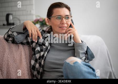 Woman Sitting On Sofa At Home Talking On The Phone Stock Photo