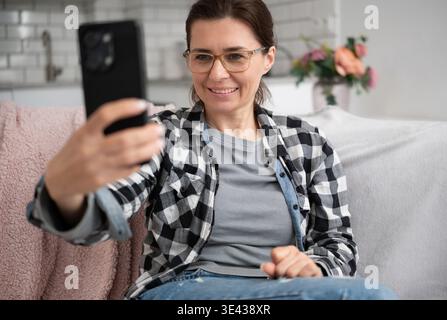 Young Woman Sitting On Sofa Having A Video Call On Phone Stock Photo