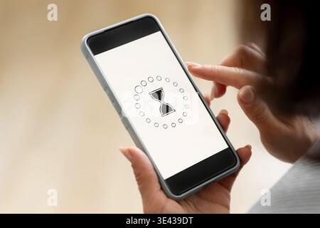 Girl Holds A Smartphone Displaying A Rotating Hourglass To Indicate A Loading Process Stock Photo