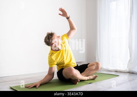 Sporty Young Man Practices A Yoga Routine And Does Core Stretching While Sitting On The Floor At Home Stock Photo