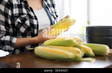 Woman Cooking Fresh Raw Corn By Peeling Fresh Corn Cobs For Boiling In The Kitchen Stock Photo