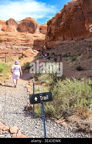 Moab, Utah, USA - 25 May 2025: Sign for a walking trail with people on the path through the red sandstone mountains near Moab in Utah. Stock Photo