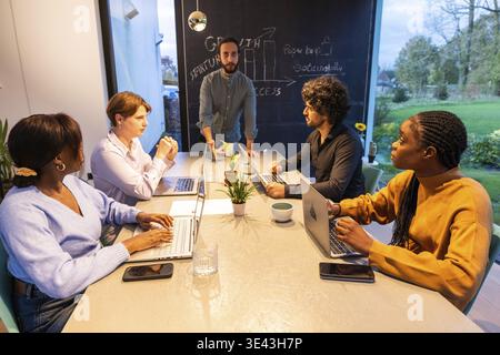 Diverse team in a modern office environment, collaborating on a project with laptops and engaging discussion Stock Photo