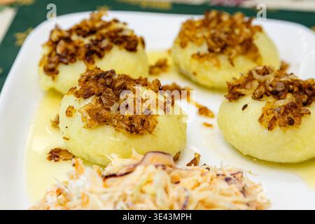 Traditional Polish pyzy dumplings with meat filling served on a plate with fried onions and a side of salad. Stock Photo