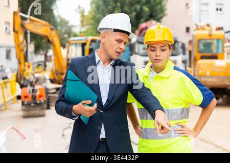 Civil engineer discussing a construction plan with a young woman worker shows her something Stock Photo