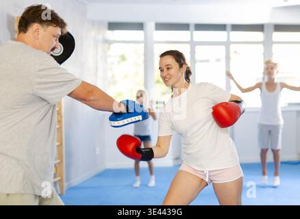 Positive woman in boxing gloves practicing punches on mitts with husband Stock Photo