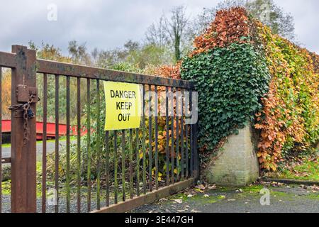 Warning sign on a closed gate with autumn foliage surrounding the area. Concept of restriction, danger, and private property Stock Photo