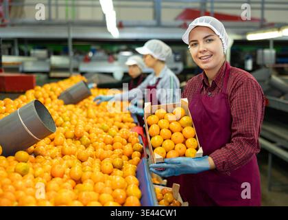 Happy female sorting factory worker showing mandarins in box Stock Photo
