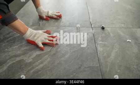 Close up of a construction worker installing large format ceramic tiles on a floor. Using a tile leveling system for a professional finish. Home renov Stock Photo