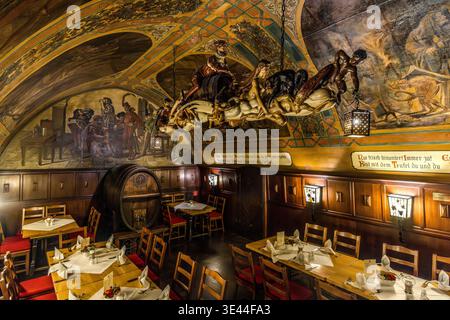 Dining room at Auerbachs Keller in Leipzig: tables laid with white tablecloths and red chairs beneath a barrel vault adorned with figurative murals from Goethe’s *Faust*, a Baroque sculpture group and an old wine barrel. Leipzig, Saxony, Germany Stock Photo