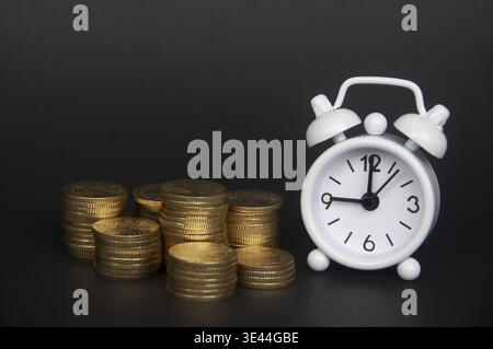 White alarm clock with gold coins isolated on dark background. Copy space and business concept Stock Photo