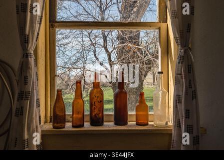 Old beer bottles on a window sill reflecting the soft morning  light in a old farmhouse. Stock Photo