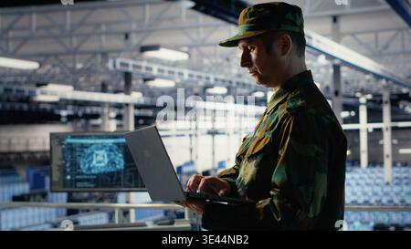 Soldier in server hub using laptop to deploy AI tech, modernizing defense infrastructure. Military data center specialist integrating artificial intelligence technology using notebook, camera B Stock Photo