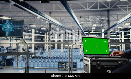 Data center employees check AI dashboard using green screen laptop during systems review. Server hub workers test artificial intelligence tools on mockup notebook for reliable performance, camera A Stock Photo