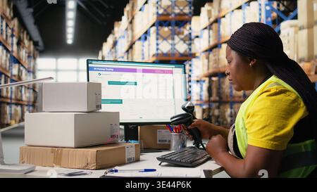 Black employee scanning awb tags after packaging operations in a distribution center, using a scanner to register barcode shipping labels for future order tracking. Storage room. Camera A. Stock Photo