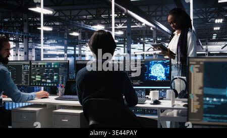 Technicians in high tech data center cooperate on neural network software development. Server hub IT workers talking, implementing deep learning technology using PC, camera A Stock Photo