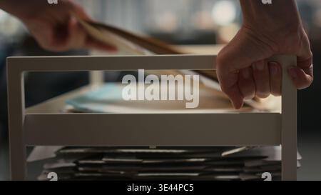 Close up of woman workplace support moves a trolley cart with folders and records, helping business employees and bringing stack of archived documents for accounting tasks. Camera B. Stock Photo