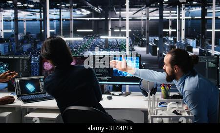 Data center team of engineers trying to fix critical error warning while using AI. Server farm teamworking colleagues repairing glitch popup while using artificial intelligence tech, camera A Stock Photo