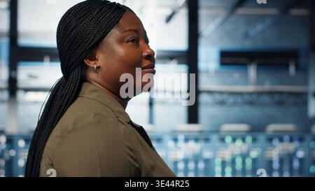 Technician in data center overseeing large scale IT gear to maintain seamless operations. IT professional walking in server hub, doing network management for increased uptime, camera B Stock Photo