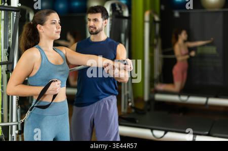 Young woman doing arm exercises and male trainer helping her Stock Photo