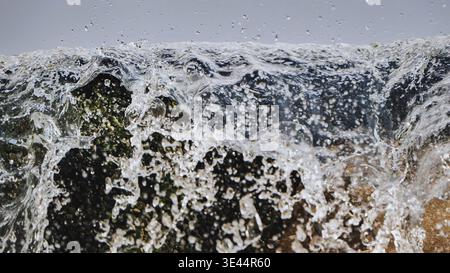 Close up of clear water splashing over mossy stones with droplets in the air Stock Photo