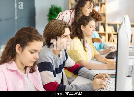 Focused teens and teacher working on computers in collaborative coding class Stock Photo