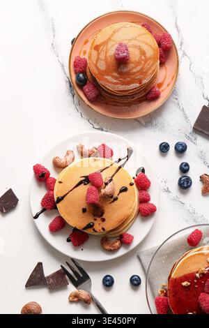 Plates of tasty pancakes with raspberries, nuts and blueberries on white marble background Stock Photo