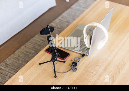 Tabletop podcasting setup showing black mic with pop filter, laptop, headphones, red phone at home Stock Photo