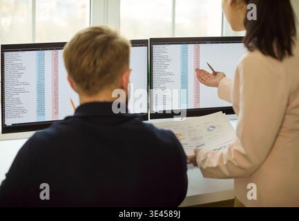 Colleagues analyzing spreadsheets on dual monitors in modern office workspace Stock Photo