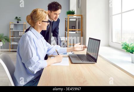 Two colleagues work in office on joint project and analyze data and plan together using laptop. Stock Photo